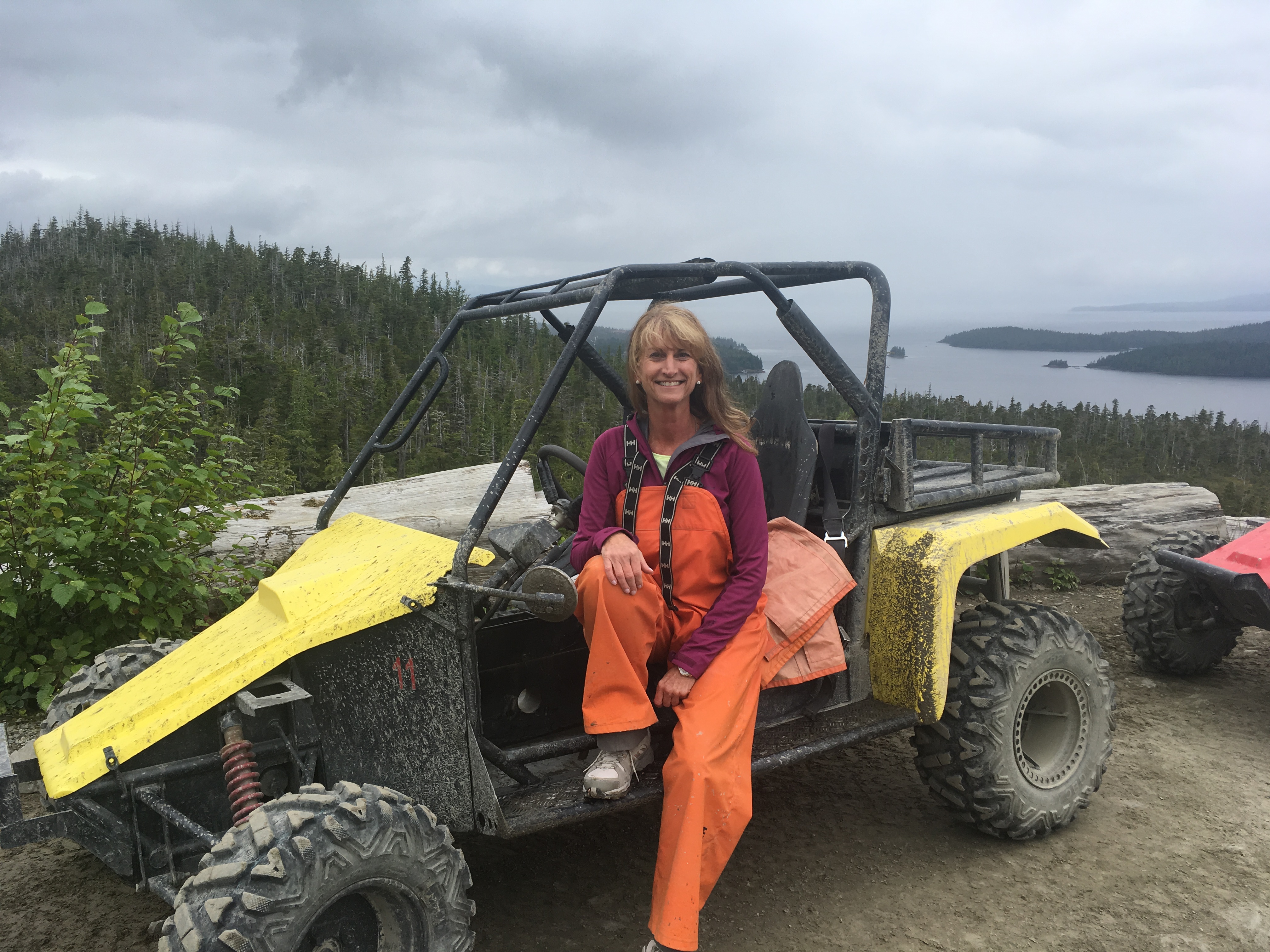 Photo of Debbie Wircenske sitting on a yellow All Terrain Vehicle (ATV) on a mountain top