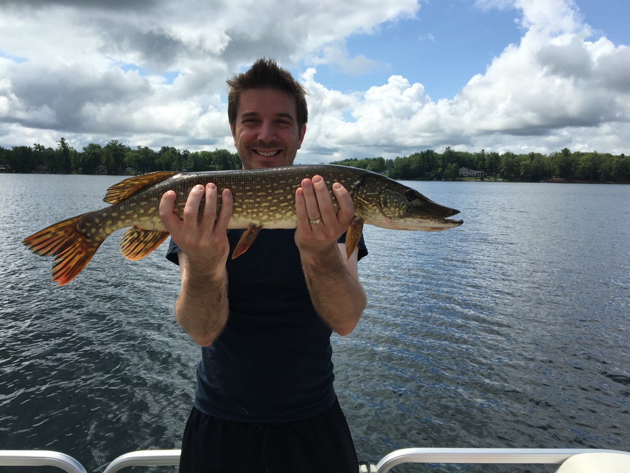 Photo of Mike Sawyers on a boat holding a Northern Pike he caught. 